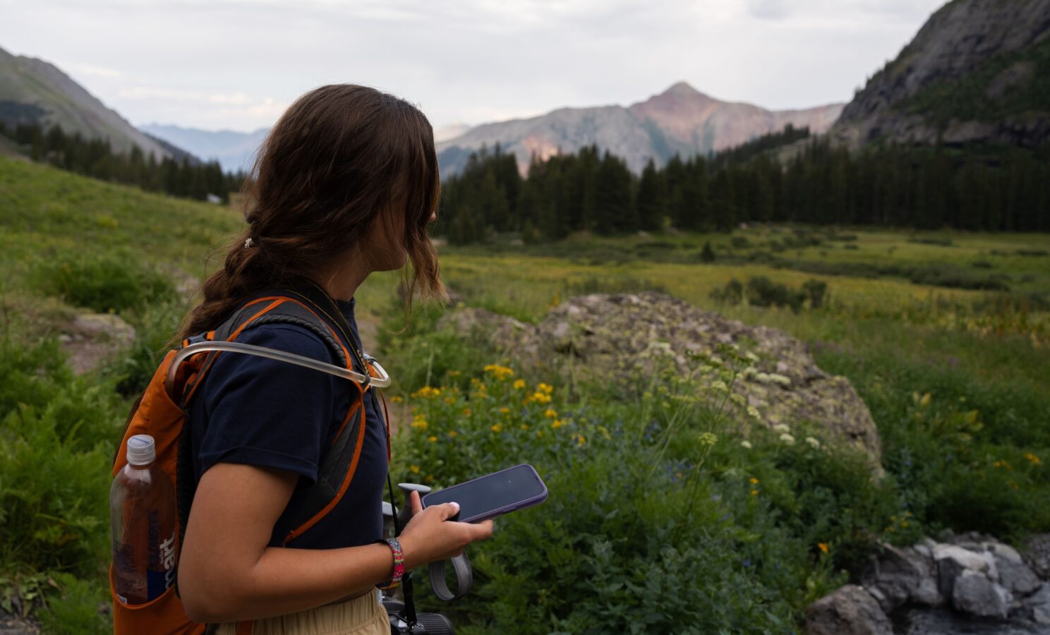 Hiker with a backpack checking the weather forecast on a phone in a mountain meadow