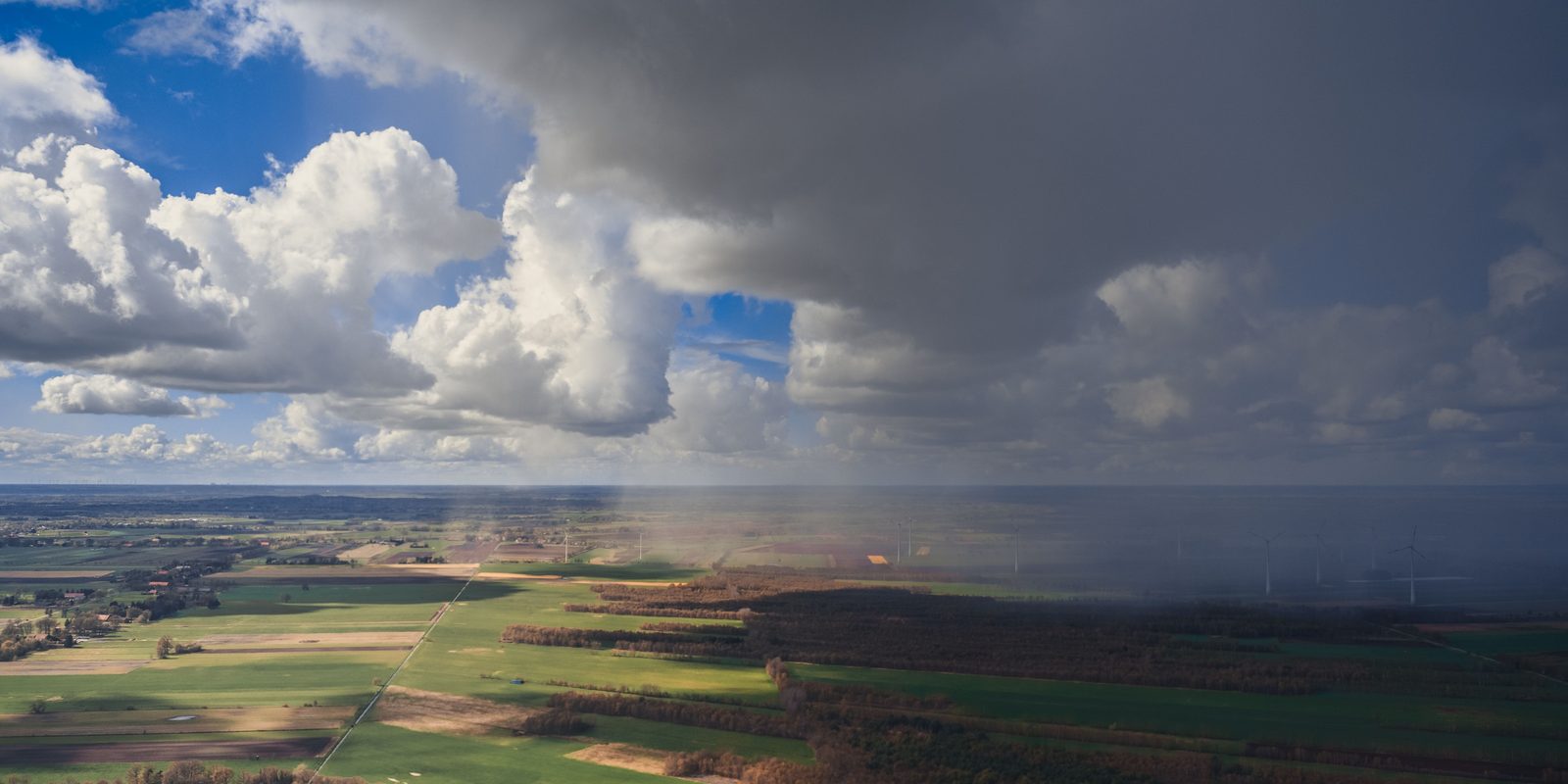 Aerial view of sunny farmland meeting an advancing rain band, showing a pressure boundary