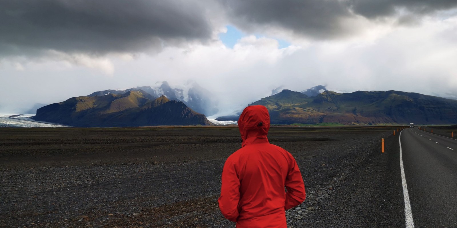 Traveller in a red waterproof jacket facing a storm over a glacier on a cold, rainy day